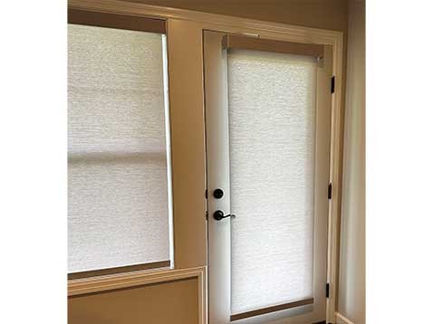 A glass door and window covered by roller shades